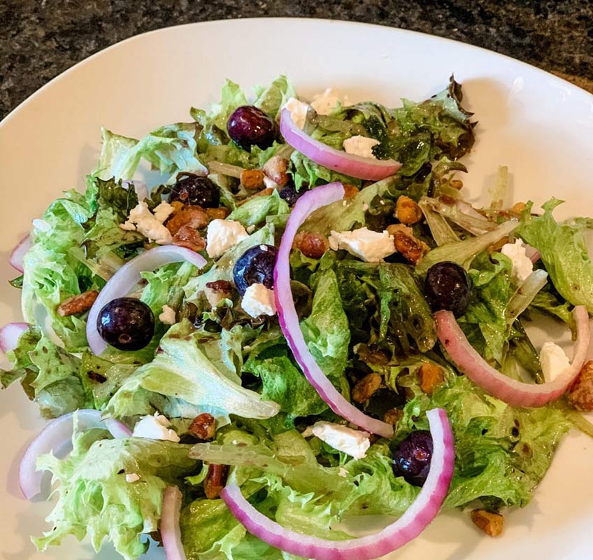 A salad with blueberries, onion, nuts, fresh veggies and dressing.