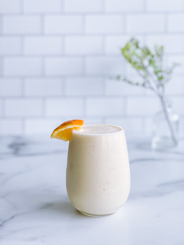 A glass of immunity boost smoothie with a decorative orange on the side of the glass.